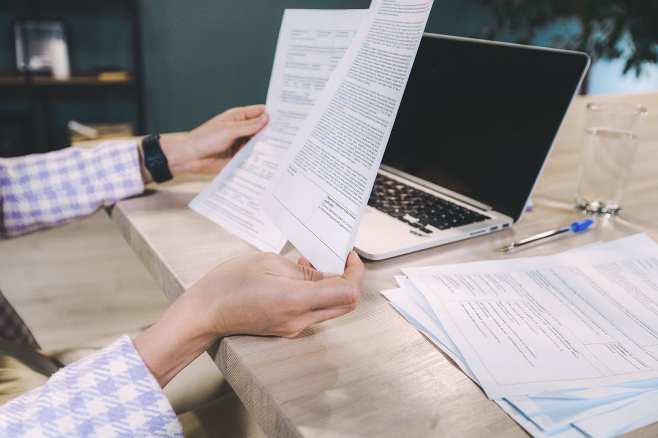 Close-up of hands examining printed documents next to laptop on office desk.