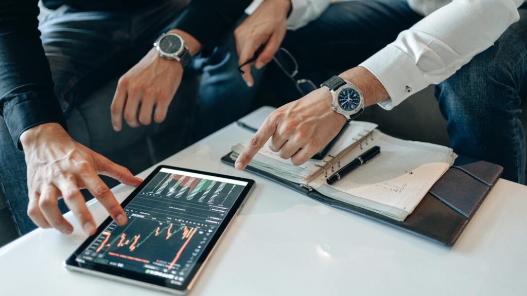 pexels-photo-5833786-5833786 Close-up of professionals discussing stock charts on a tablet with notes and pens on a table.